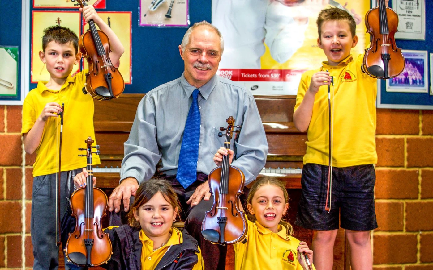 Group of Crescendo students smile while holding up their violins.