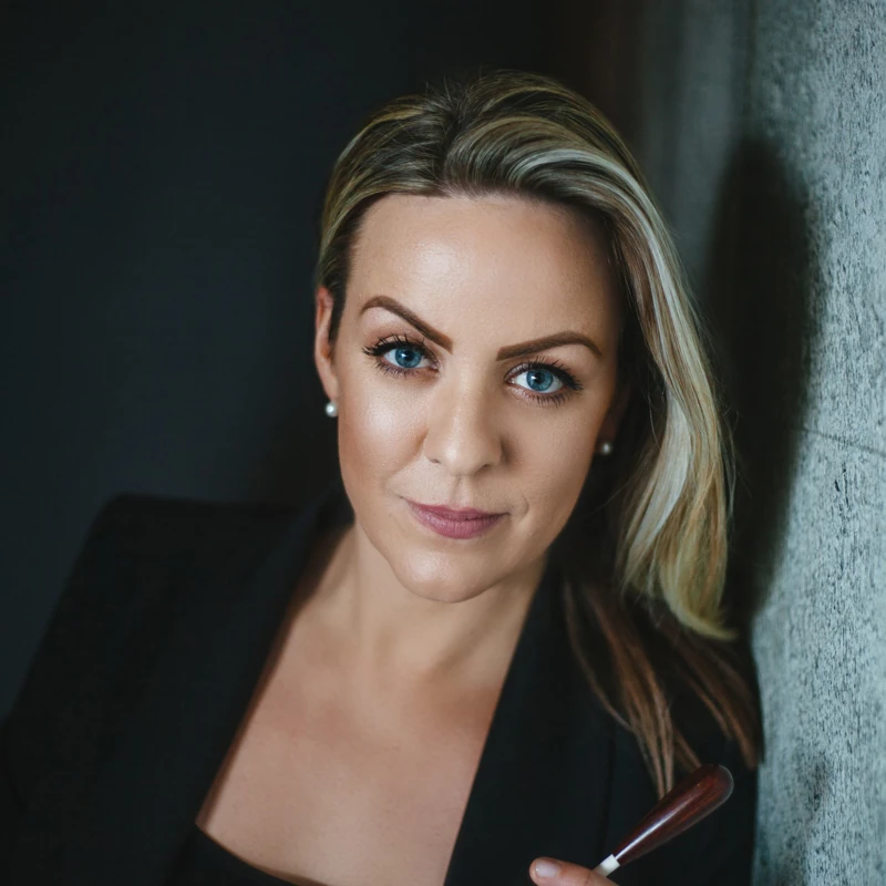 Headshot of Jessica Gethin wearing a black blazer and top, holding a baton.