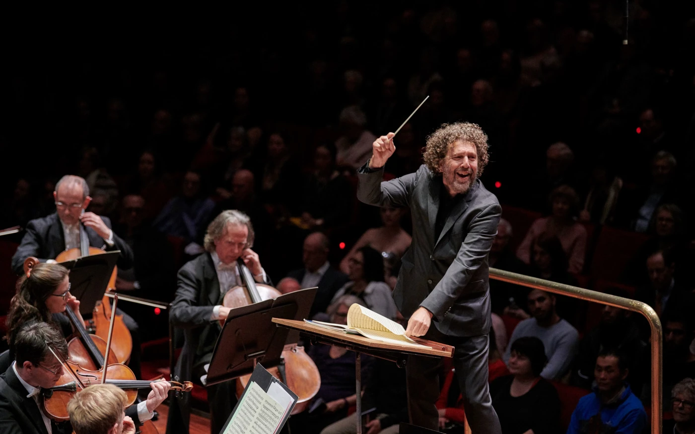 Asher Fisch smiling while conducting an orchestra.