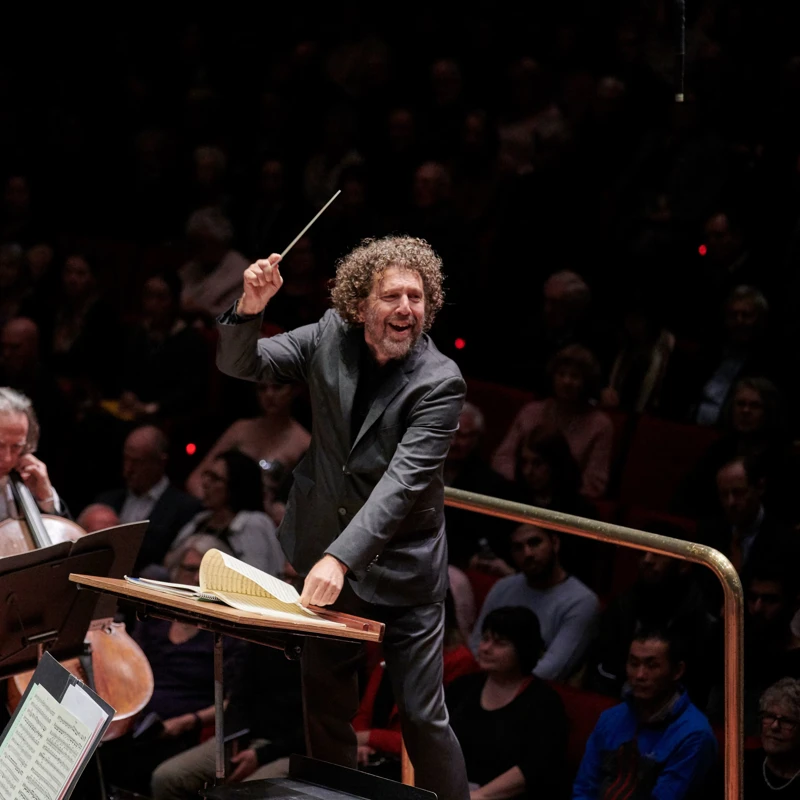 Asher Fisch smiling while conducting an orchestra.