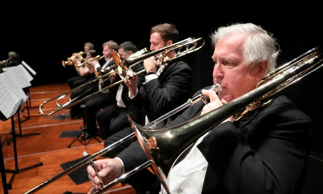 Trombone players perform together on stage during an orchestral concert.
