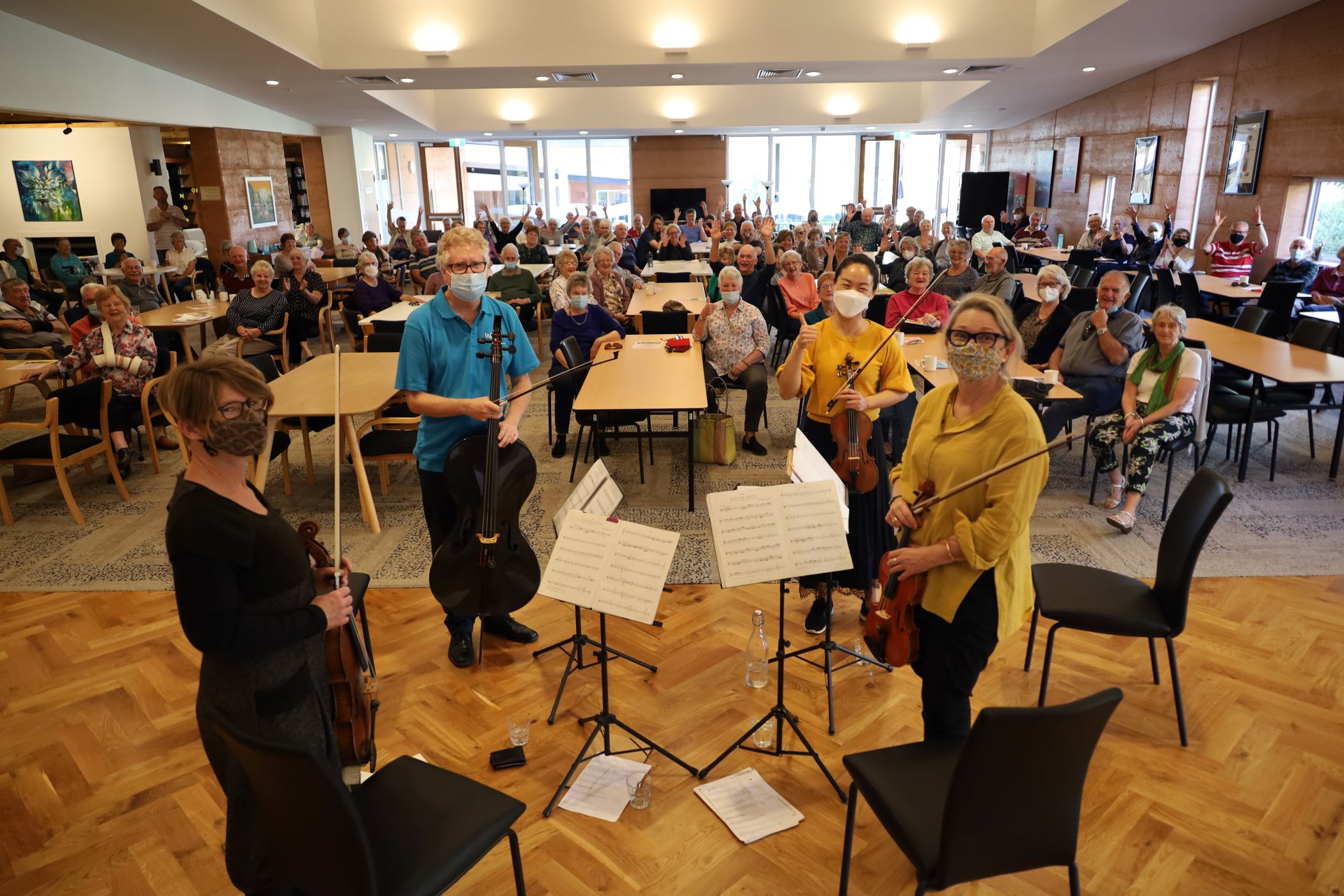 Four WASO string musicians stand before a large, joyous audience in a retirement village hall.