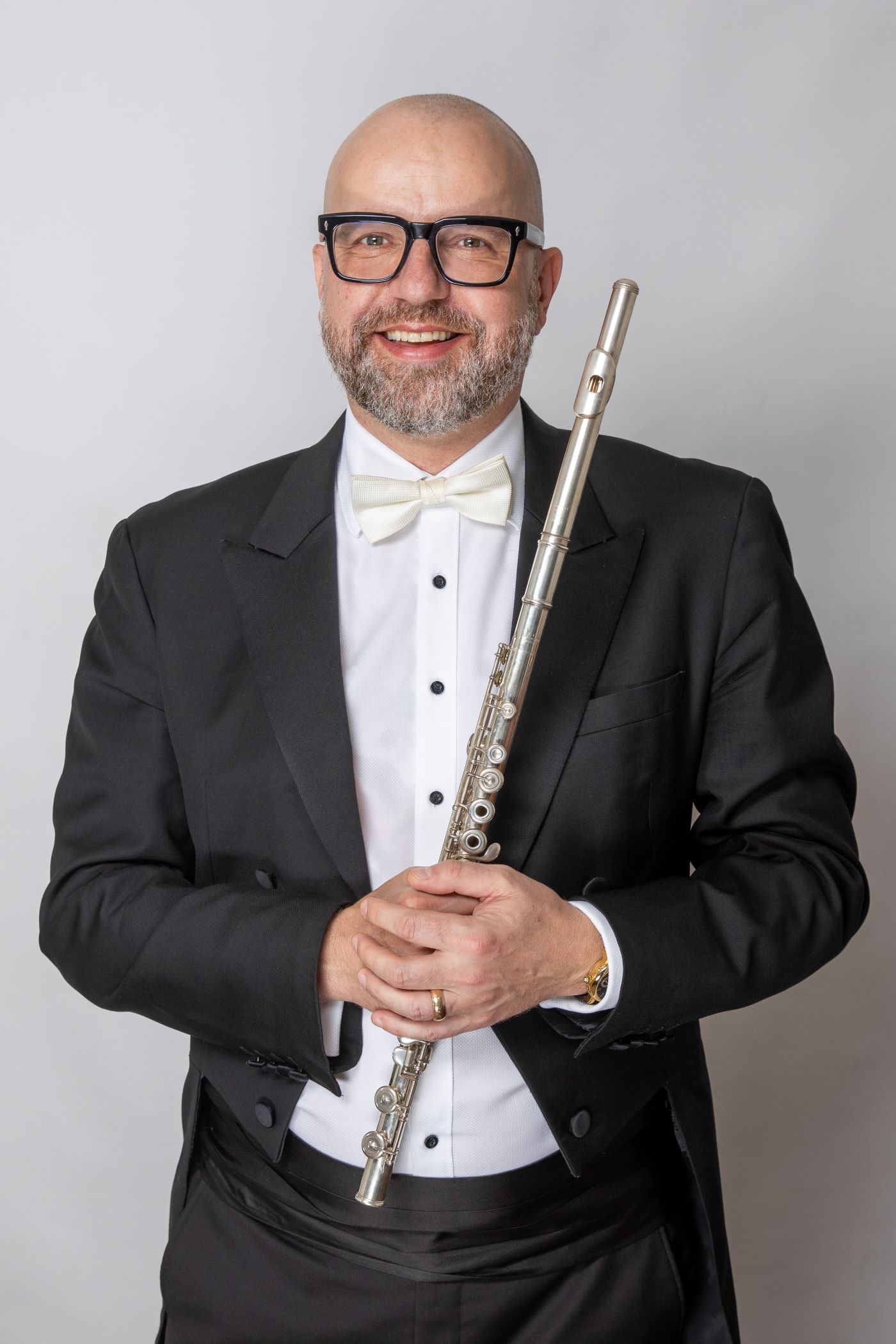 Headshot of Andrew Nicholson wearing a formal suit, holding a flute.