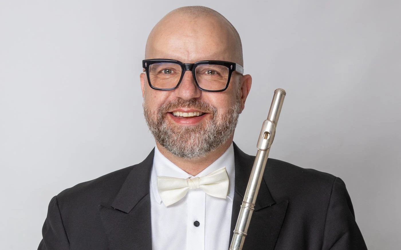 Headshot of Andrew Nicholson wearing a formal suit, holding a flute.