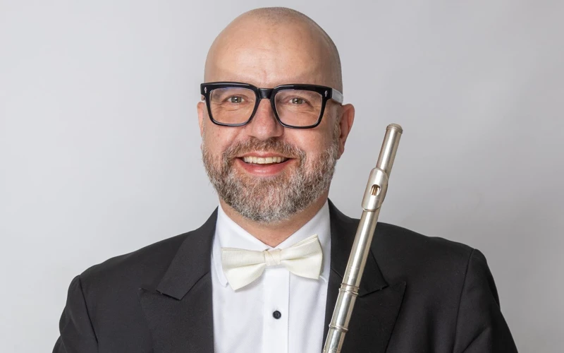 Headshot of Andrew Nicholson wearing a formal suit, holding a flute.