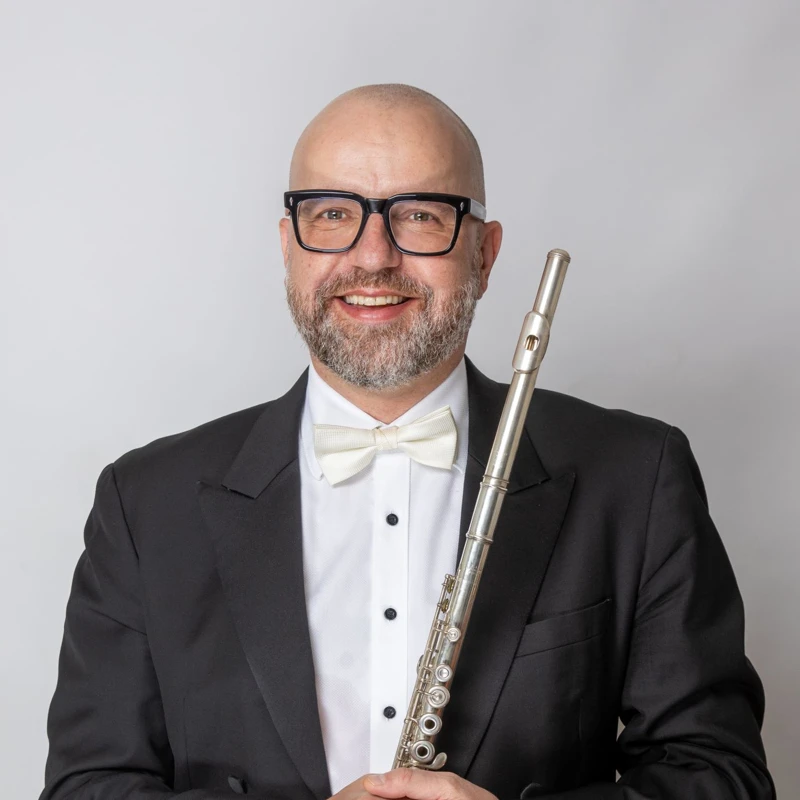 Headshot of Andrew Nicholson wearing a formal suit, holding a flute.